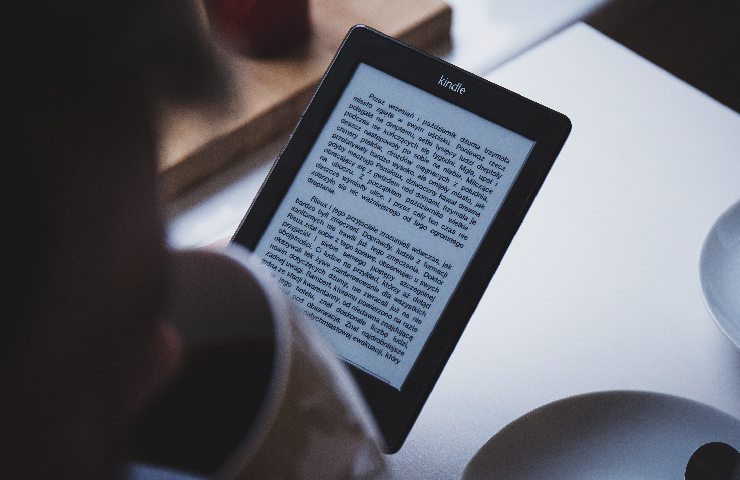 Amazon Kindle Reader messo a fuoco e tenuto in mano da qualcuno che tiene anche una tazza da bere